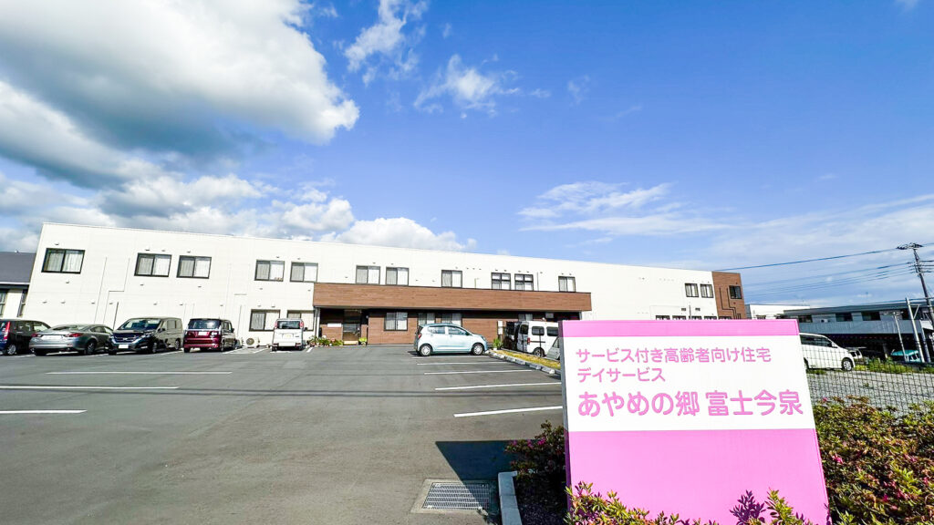 ピンク色の看板が目立つ介護施設の建物外観と駐車場